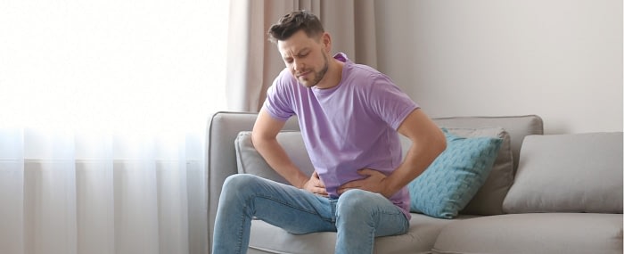 Young man sitting on couch holding his stomach in pain
