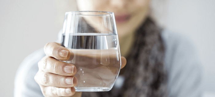 A woman holding a glass of water to promote gut health