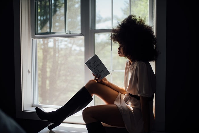 Girl sitting by an open window reading self care book