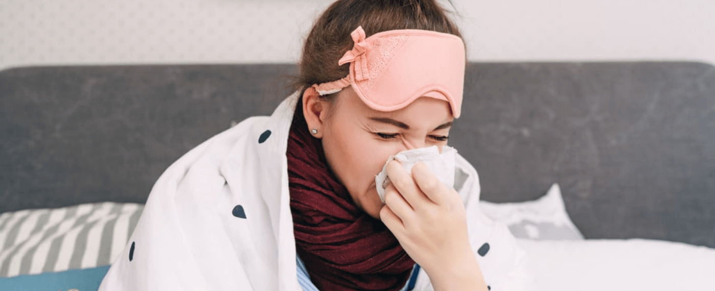 woman sick in bed blowing nose into tissue