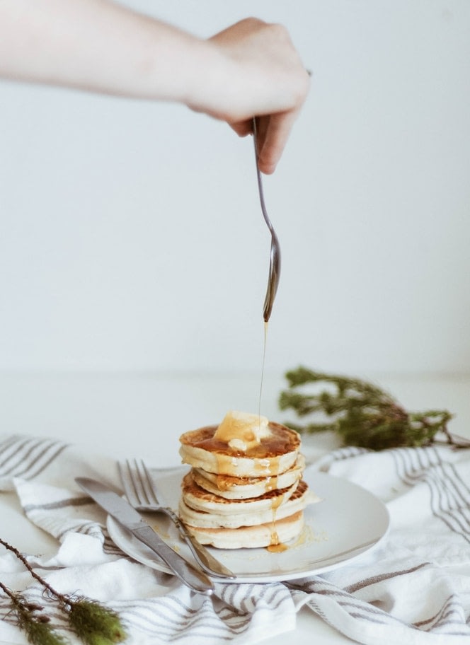 A spoon dripping cbd honey over a short stack of pancakes