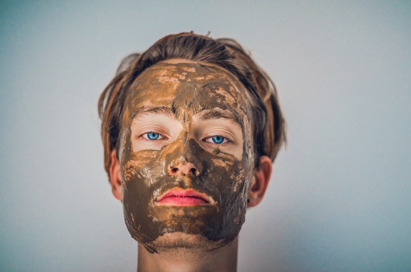 a woman using a mud face mask as part of her skin care routine