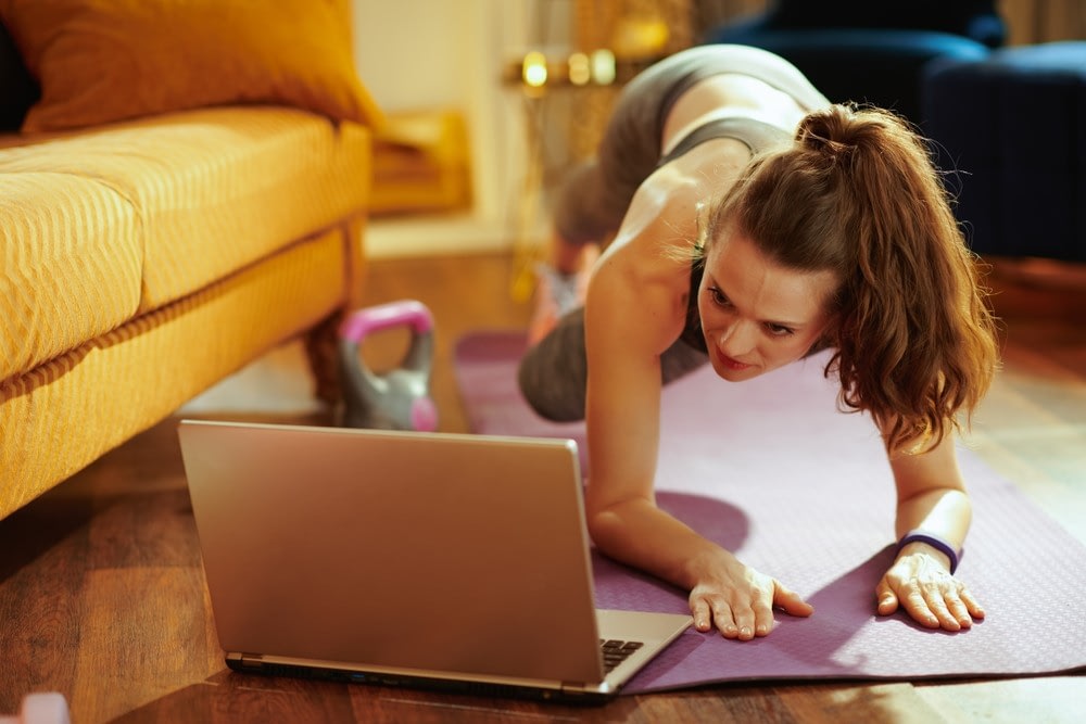 Woman using laptop and apartment to practice yoga