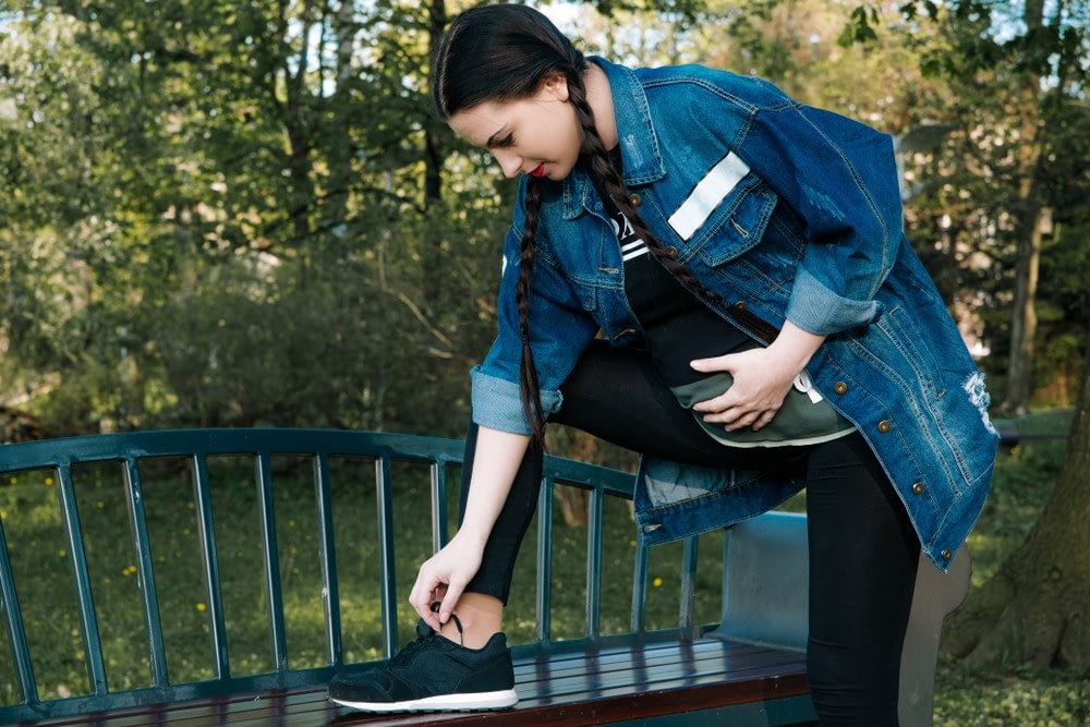 Pregnant woman bending over park bench to tie elastic shoelaces