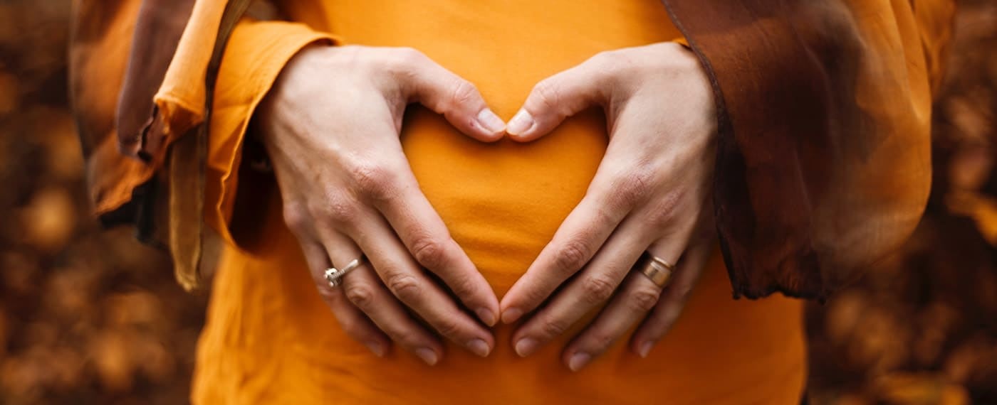 Woman's hands making the shape of a heart over pregnant belly
