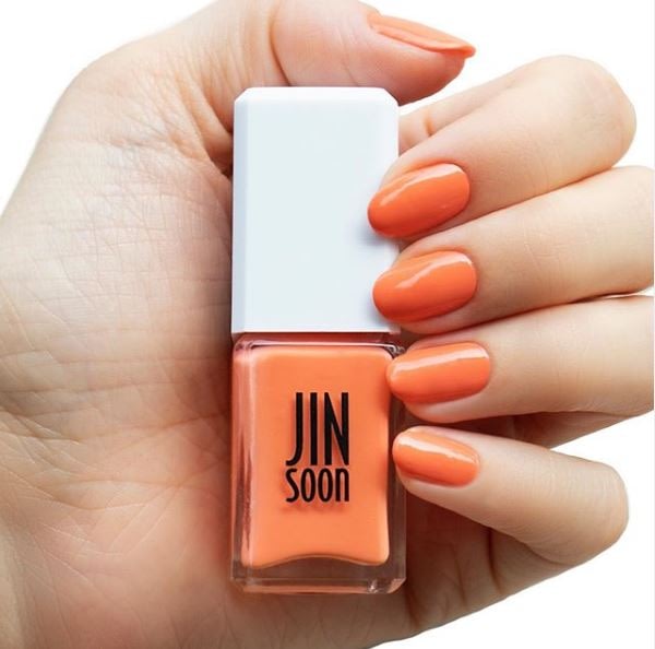 Female hand with bright orange nails holding a bottle of Jin Soon nail polish