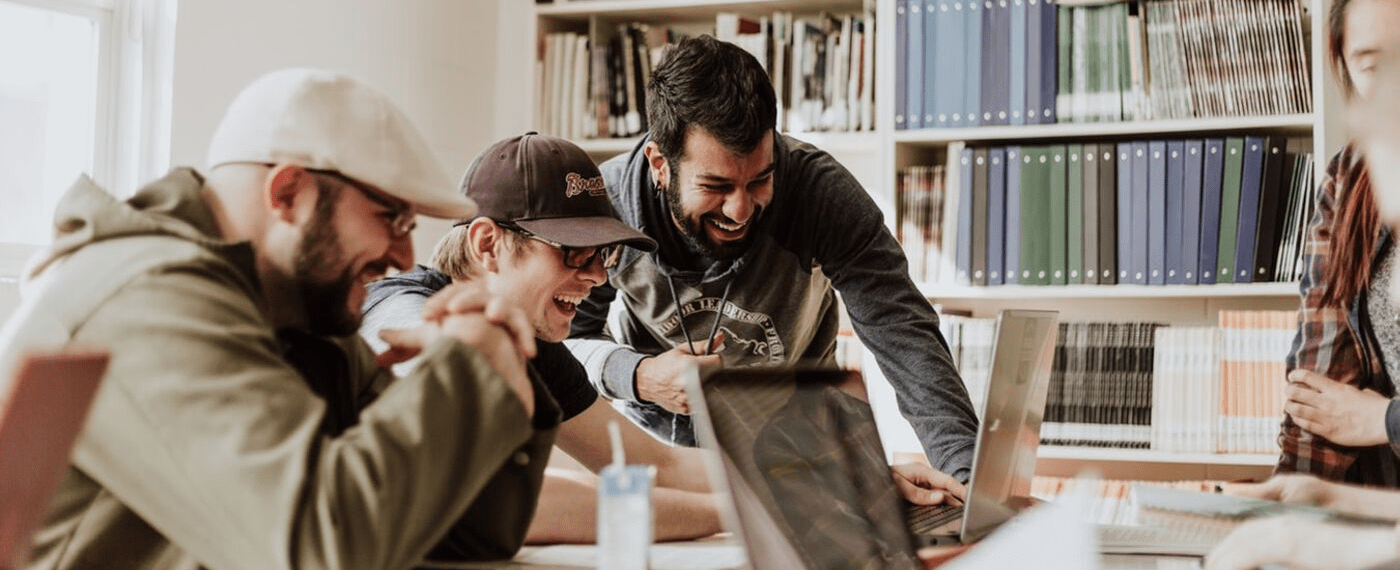 3 male students laughing and studying in library