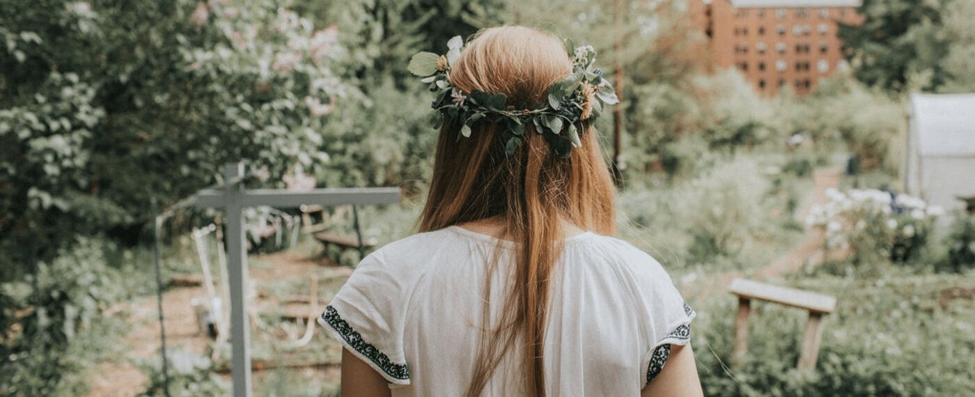 girl wearing a crown of leaves looks out at a field of wild flowers of bushes