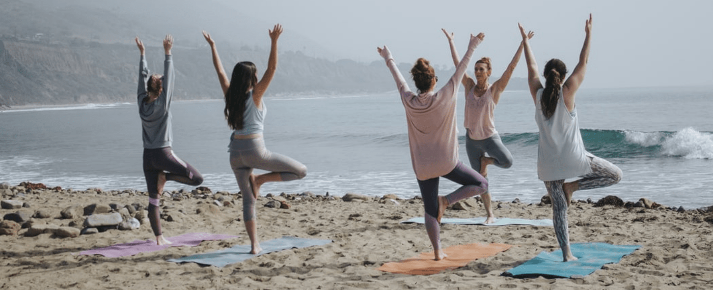 Female yoga instructor teaching a group of women yoga on the beach