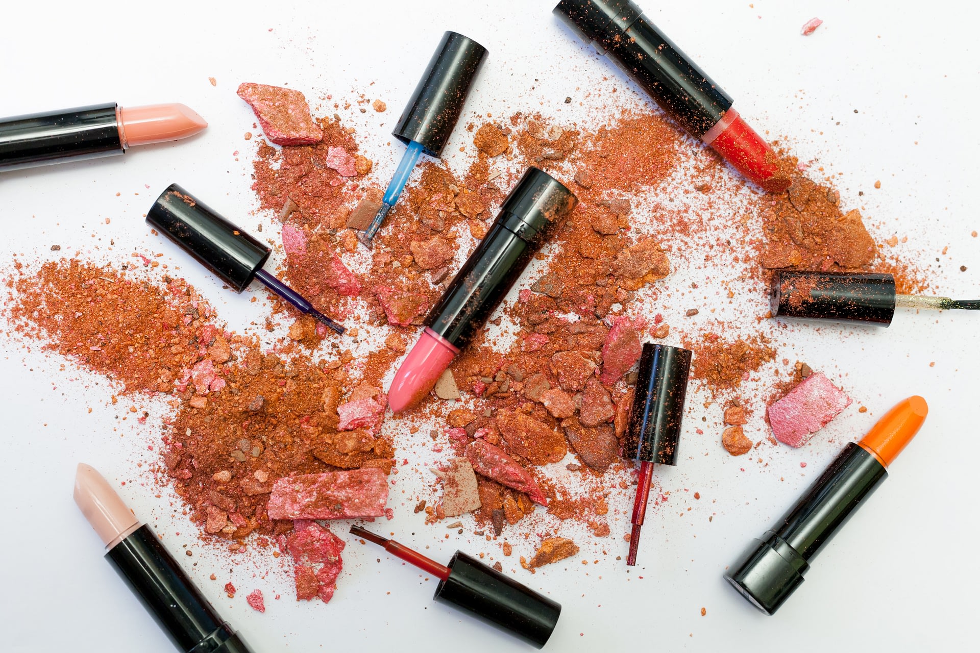 Lipstick and nail polish scattered around broken makeup