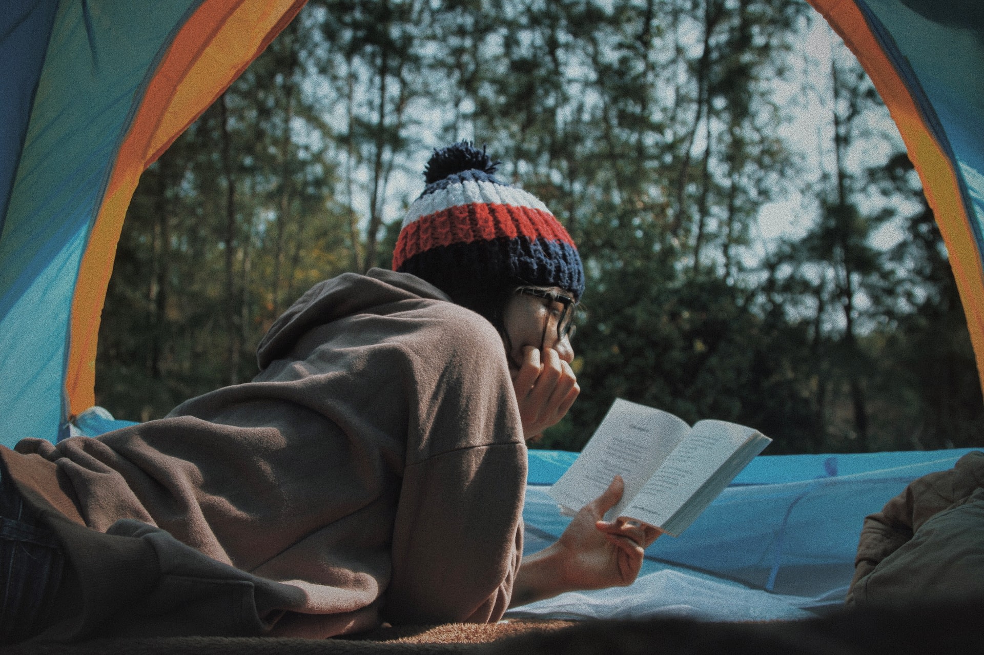 Girl reading a self-help book inside a tent while camping outdoors