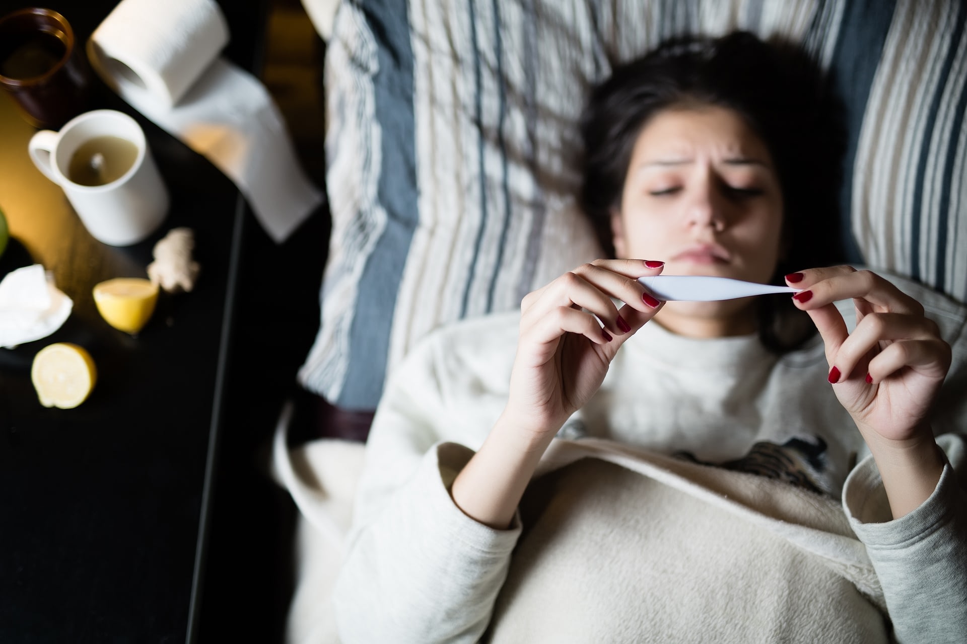 Young girl lying bed with flu looking up at thermometer