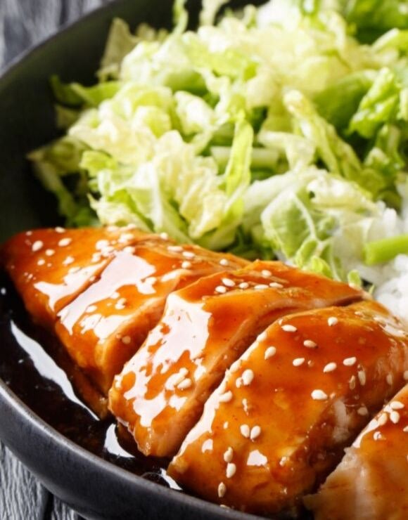 A plate of glazed teriyaki chicken with sesame seeds and greens