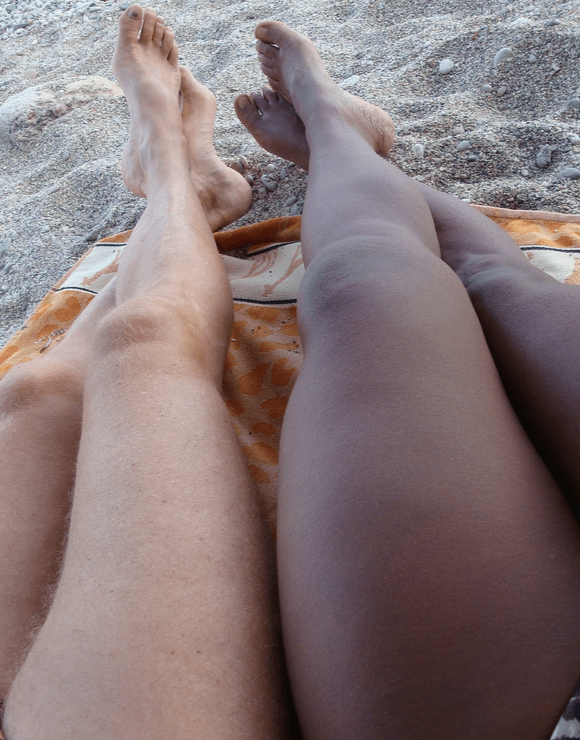 two sets of legs laying in the sand on a beach