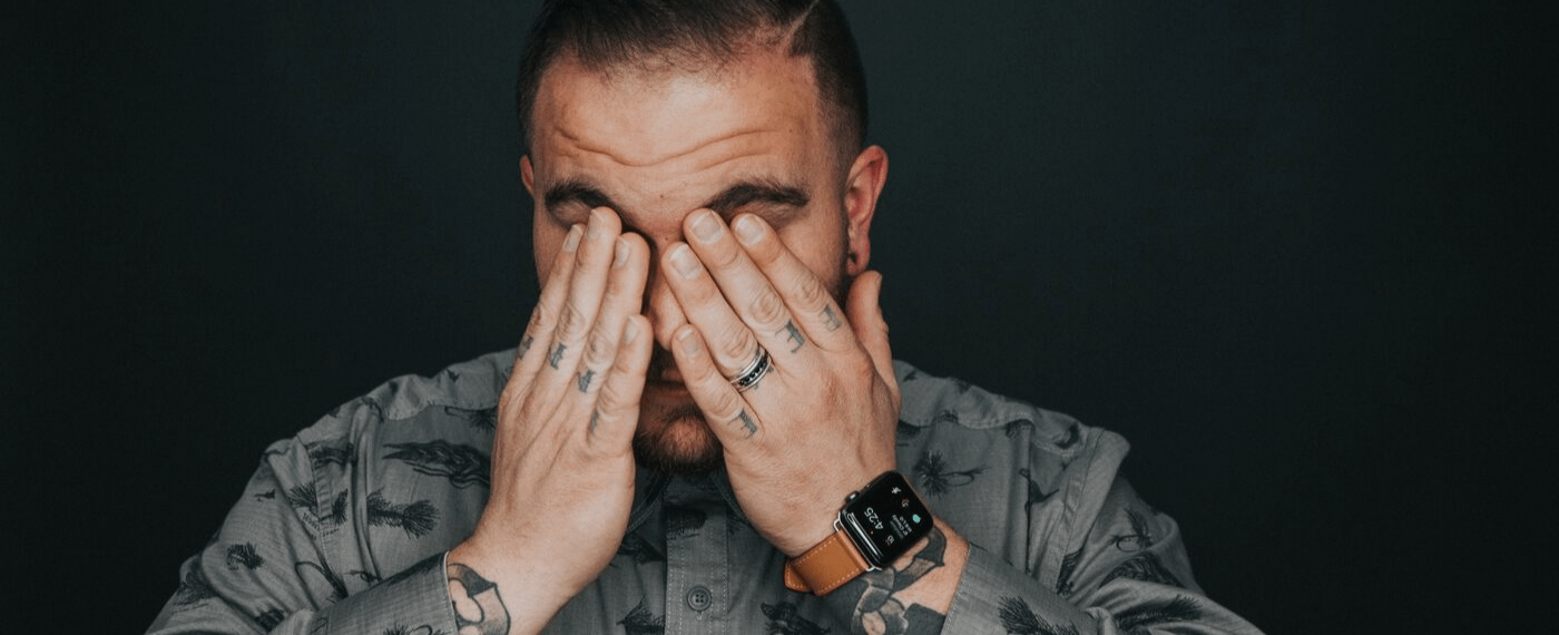 Man with tattoos suffering from a migraine covering his face