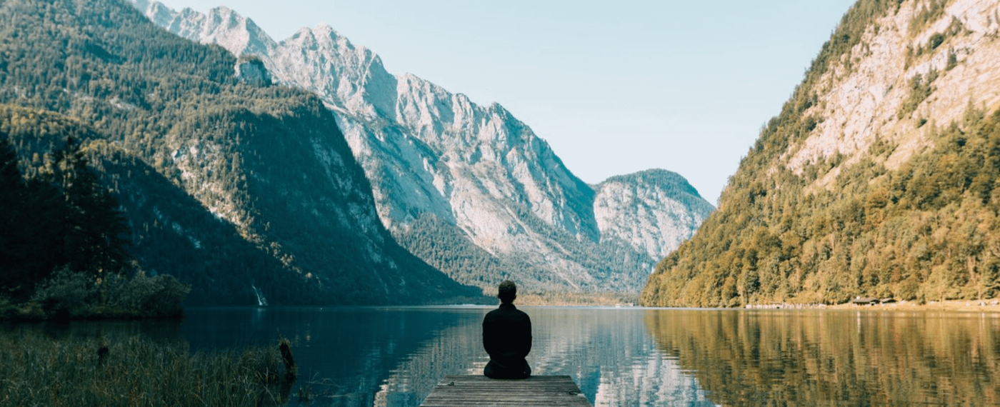 Man sitting on the dock of a lake looking at mountains