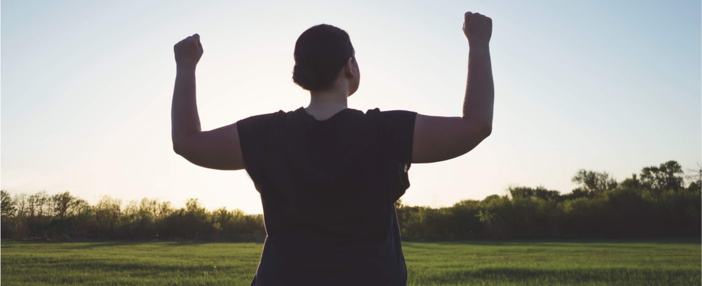 Woman standing in a field with her arms raised in power