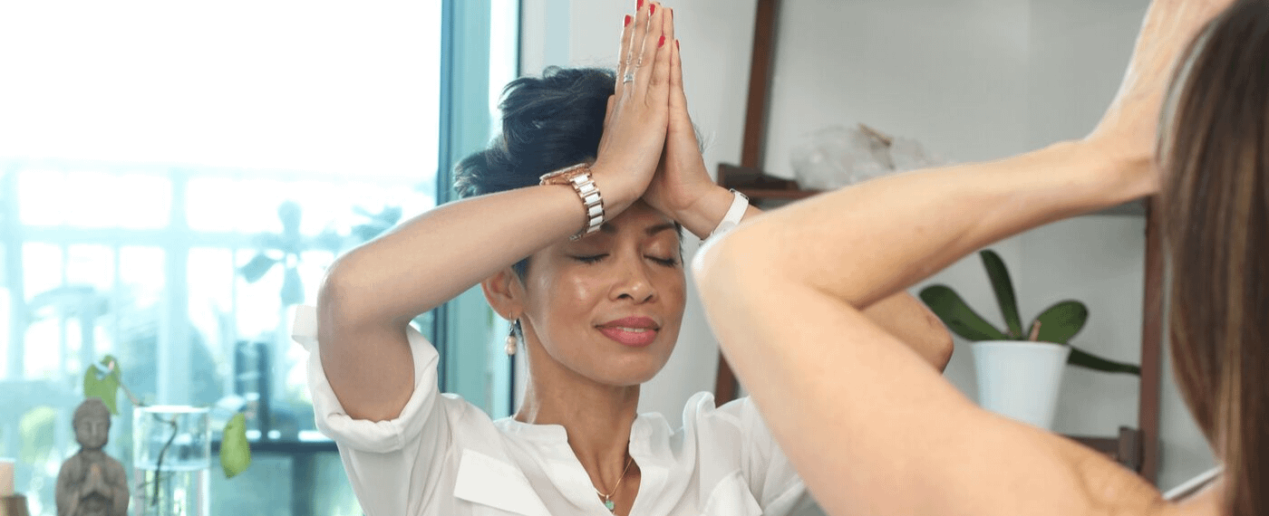 Woman dressed in white meditating with hands at forehead