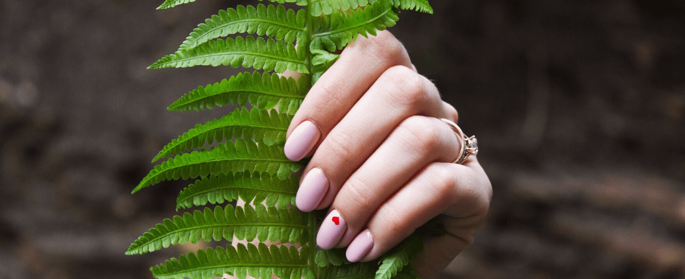 Manicure pink nails with a small heart on the ring finger caressing a plant