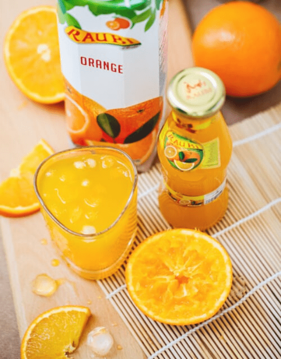 A small glass of orange juice with orange slices lying next to the glass