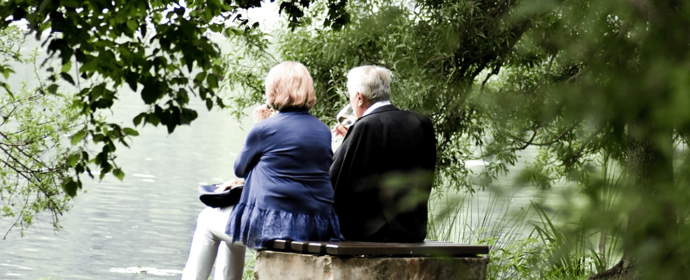 older couple sitting on park bench drinking a glass of wine