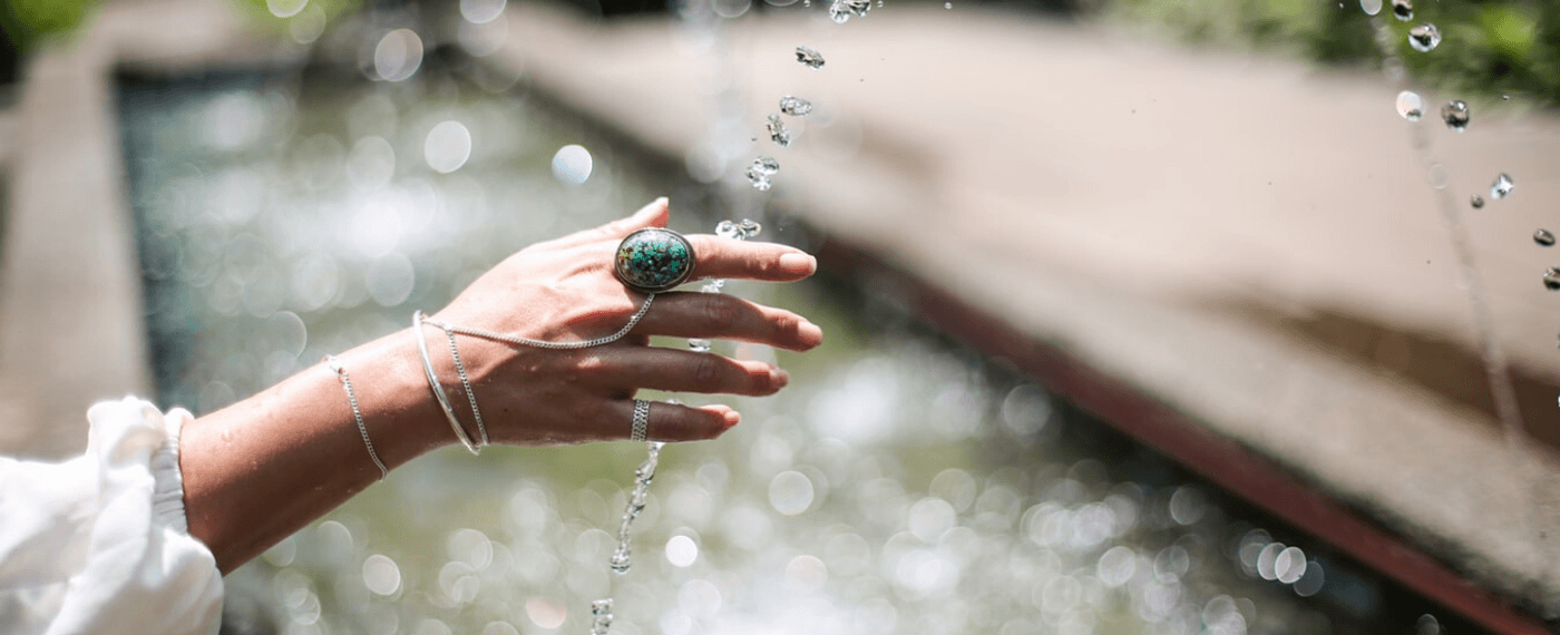 Female with healthy nails running fingers through drops of water from a fountain