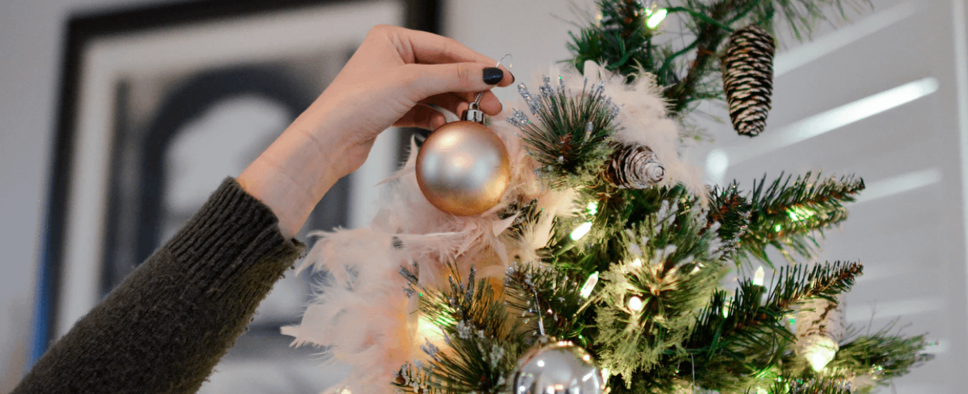 A woman hangs last-minute holiday decor on her Christmas tree
