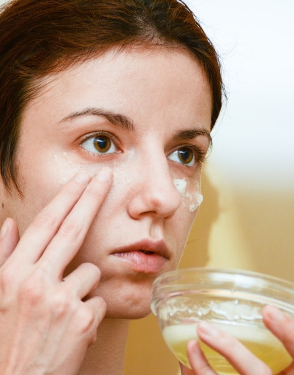 Woman applying raw egg whites to her face to help reduce baggy eyes