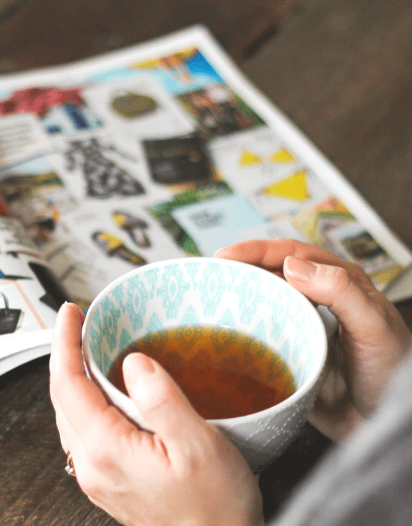 A woman drinks tea while looking at a catalogue