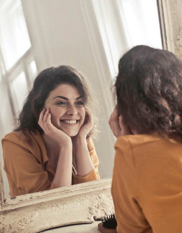 woman leaning on elbows smiling at her reflection in the mirror