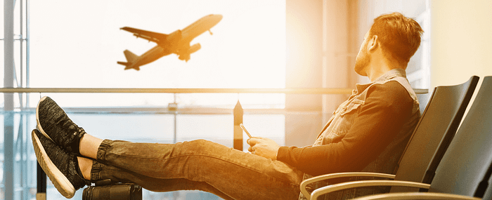 man waiting in airport terminal staring out the window at plane taking off