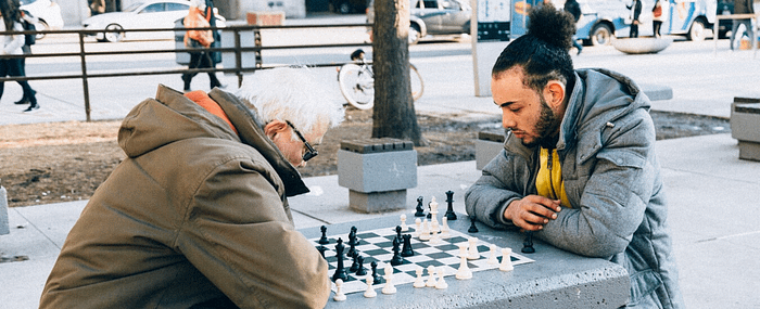 Older man playing chess in the park with a younger male