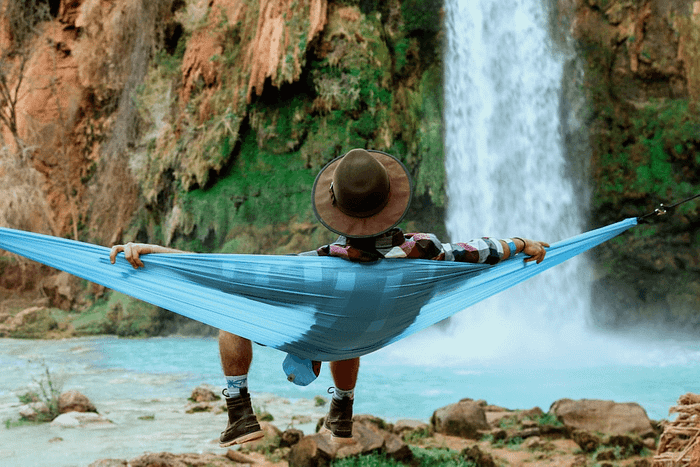 woman sitting on hammock in front of waterfall relaxing to the calming effects of water