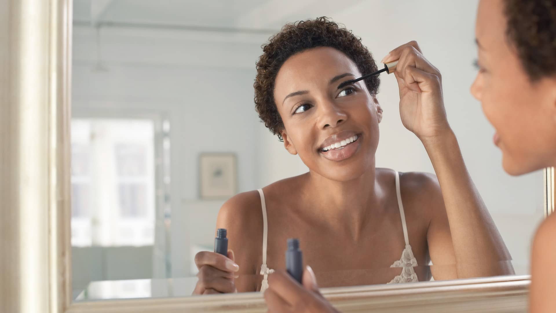 woman applying mascara in mirror using makeup tips