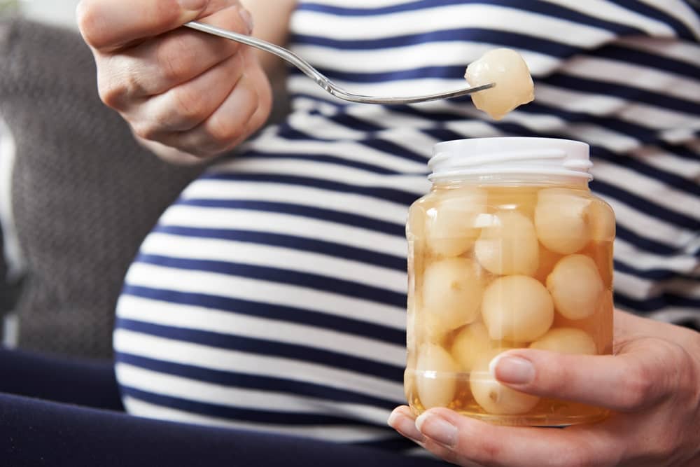 Pregnant woman eating jar of fruit because of pregnancy cravings