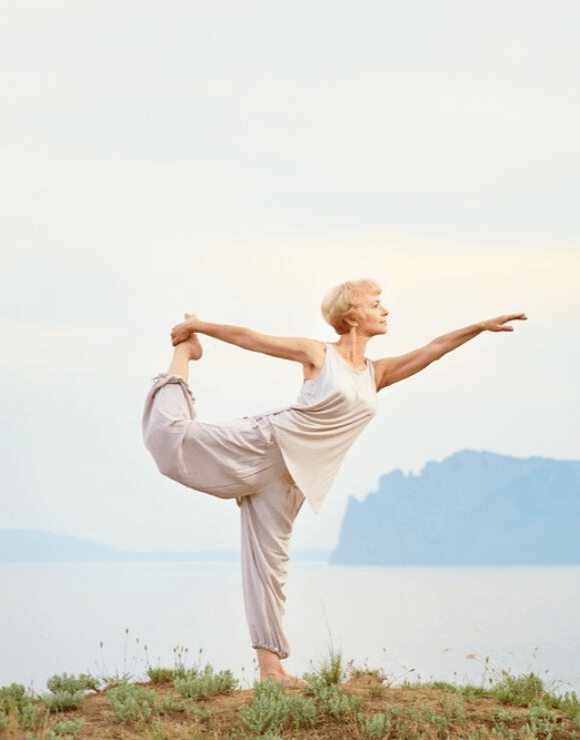 Older woman practicing the natarajasana yoga pose a top a hill
