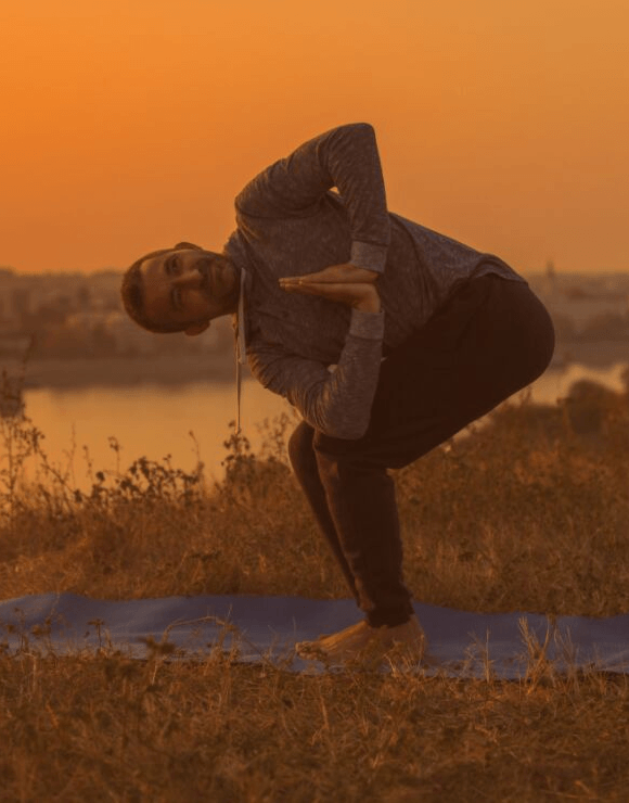 Man in a field practicing the Prayer Twist Yoga Pose