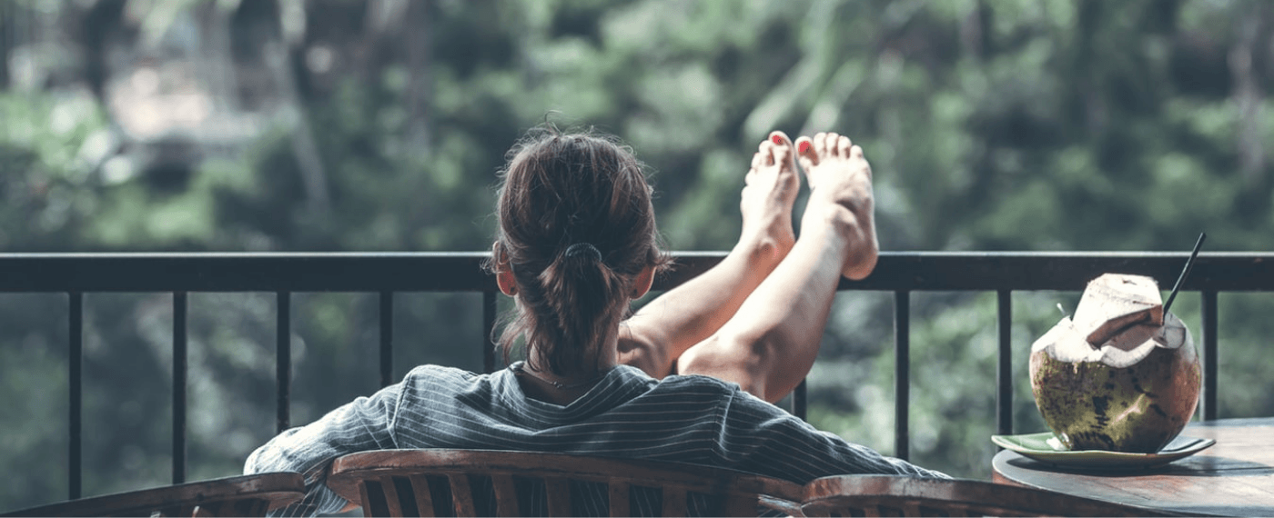A woman sits reclining on a balcony, staring out into nature