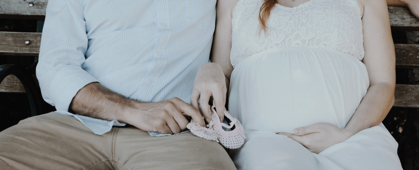 Husband and wife sitting on a bench holding baby shoes discussing how pregnancy affects fathers