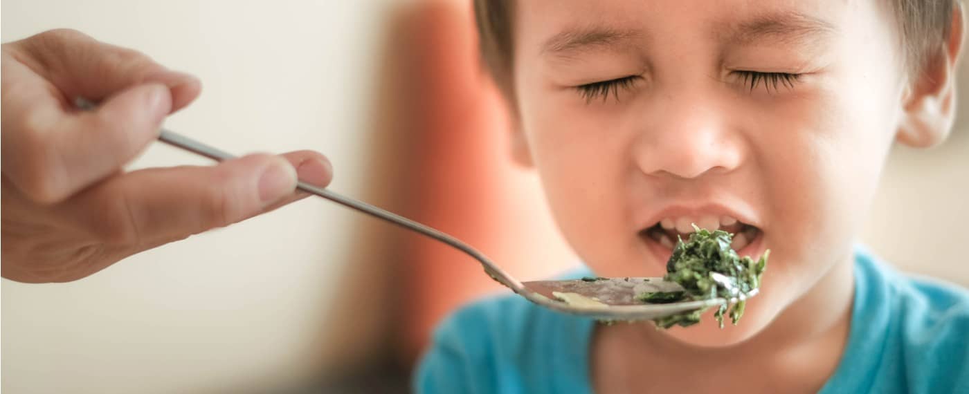 A child grimacing while being fed green vegetables