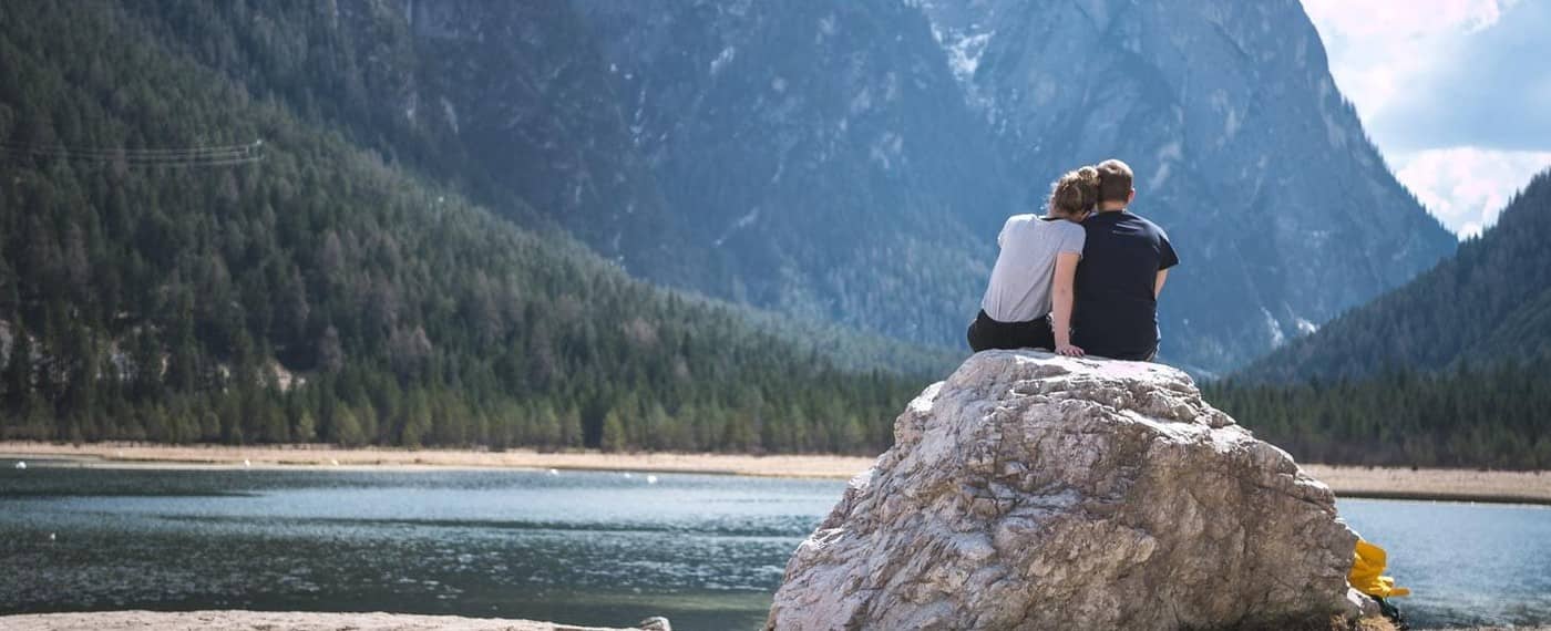 A couple sits enjoying an intimate moment on a rock by a lake
