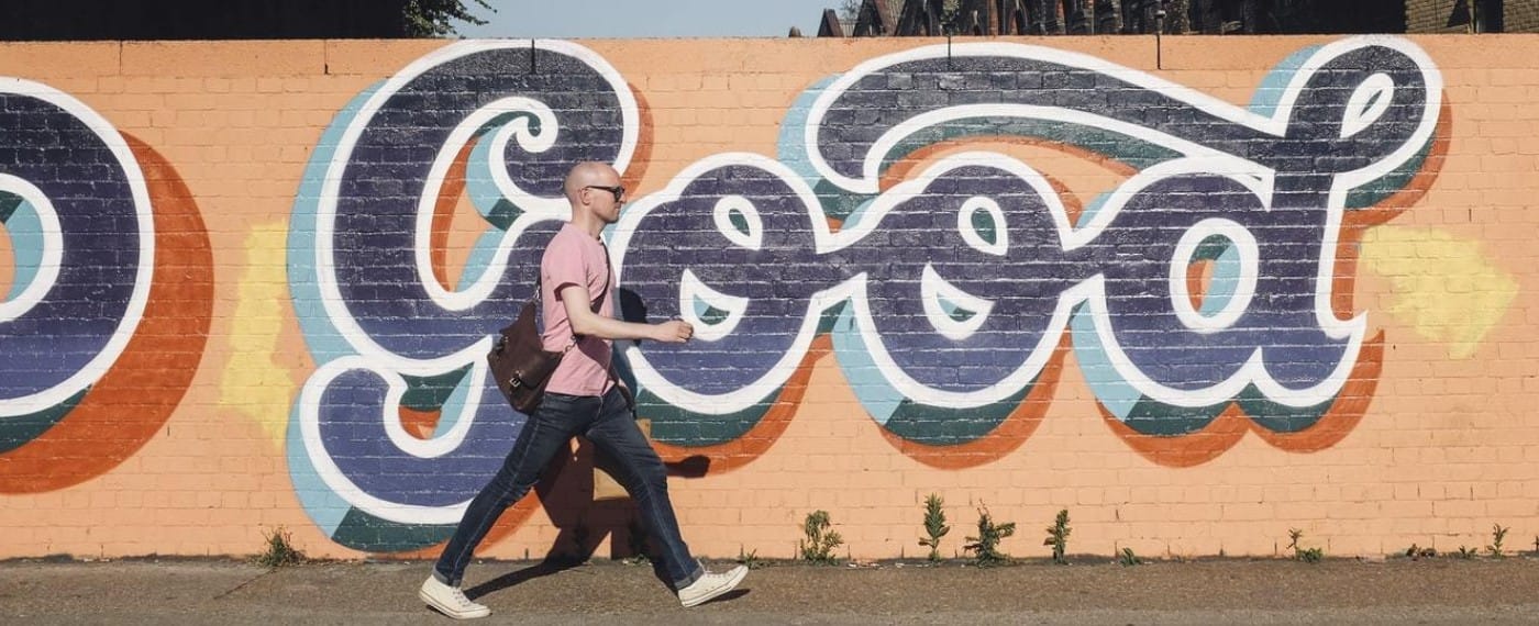 A bald man walks purposefully along a wall with graffiti