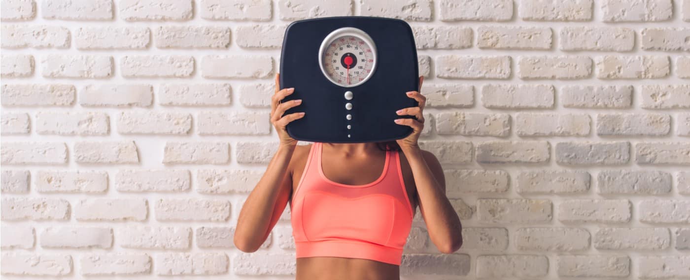 woman in fitness attire holding scale for losing weight