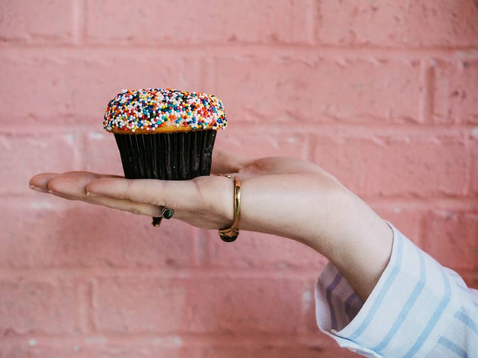 A hand held out holding a cbd cupcake with sprinkles