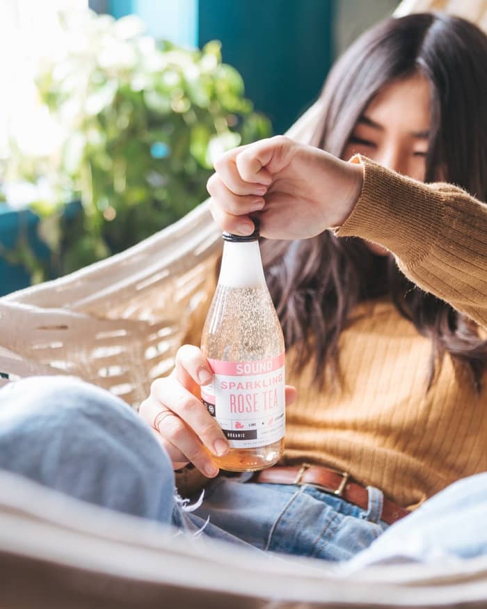 Young girl twisting the cap off a rose pink cbd sparkling water
