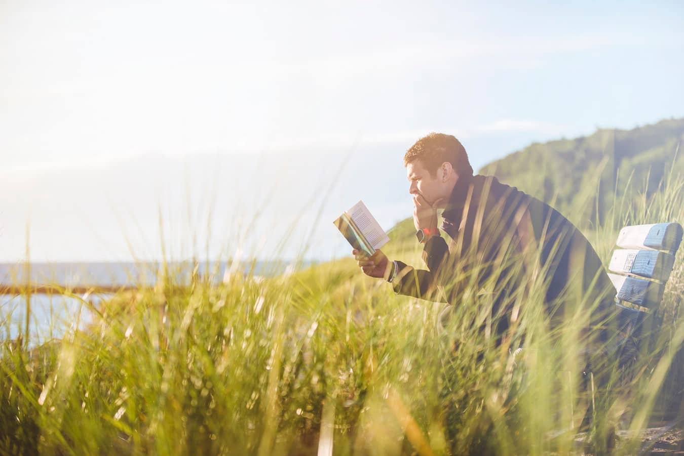 Healthy man reading a book while sitting on a bench in a field