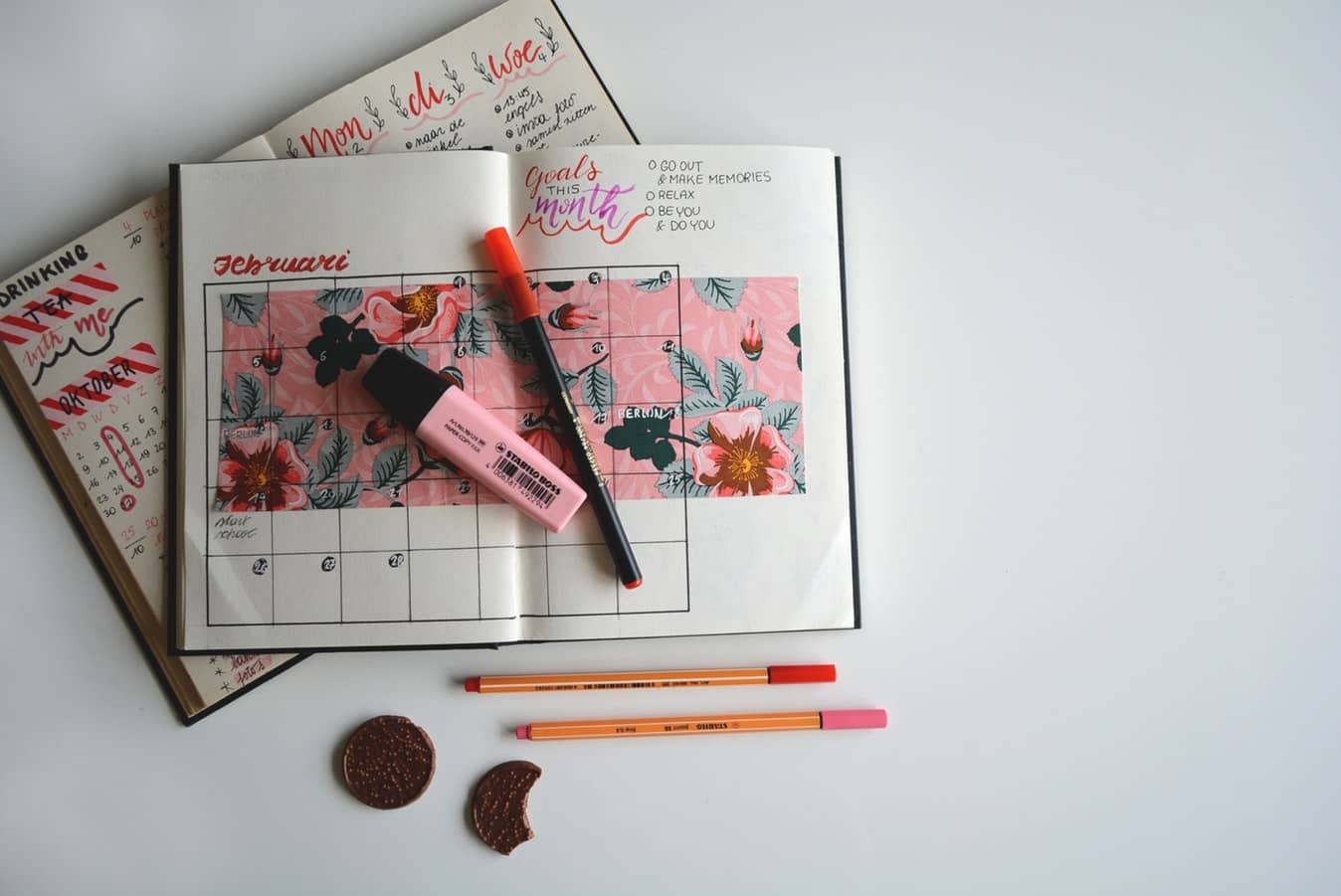 A goal calender open on top of a daily planner with a highlighter and pencils