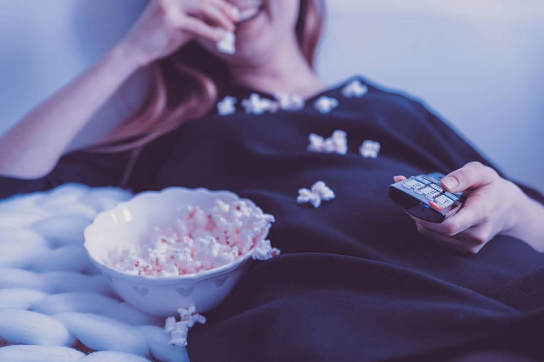 Woman laughing while eating a bowl of popcorn and watching tv