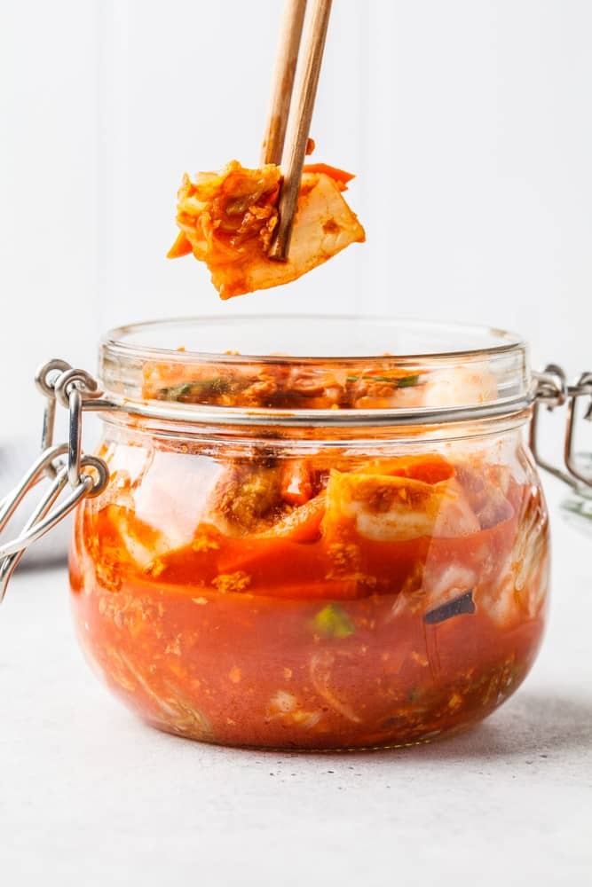 A piece of chutney being lifted out of a jar with chopsticks