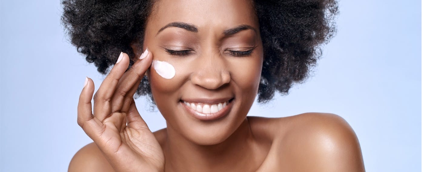 woman smiling while applying lotion to her face for skin care routine